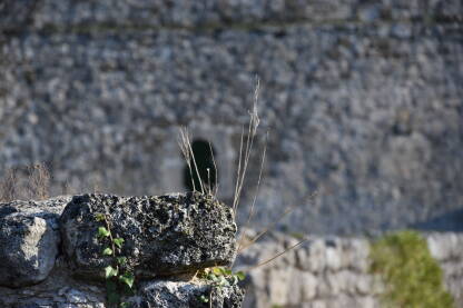 Detalj kamena i trave sa tvrđave u Jajcu sa srednjovjekovnim prozorom i jednim od bedema u pozadini.
