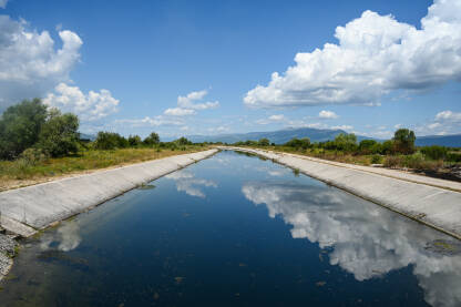 Riječni kanal u polju. Voda u kanalu. Refleksija neba i oblaka u vodi.