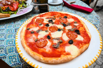 Pizza na stolu u restoranu. Pizza s sudžukom, povrćem, maslinama i sirom.