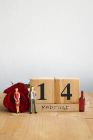 Kalendar sa datumom 14. Februar, crvenom ružom i figurama para sa flašom pića.