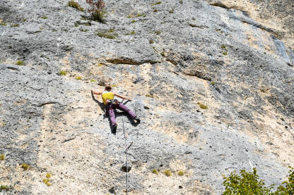 Djevojka sa užadima po penje na stijeni. Žena se penje uz okomitu stijenu na planini.