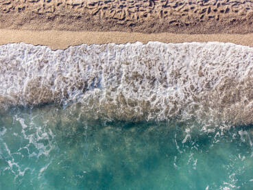 Pješčana plaža i more, snimak dronom. Prekrasna tropska plaža tokom ljeta. Snimak dronom na valove koji se razbijaju na plaži s pijeskom.   Prozirna morska voda.
