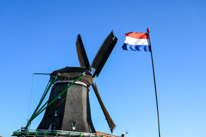 Zastava Nizozemske kod stare vjetrenjače. Tradicionalna vjetrenjača uz vodu.