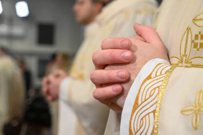Katolički svećenici u liturgijskim odorama se mole sa sklopljenim rukama. Ruke čovjeka koji se moli u katedrali. Božićna misa polnoćka u crkvi.