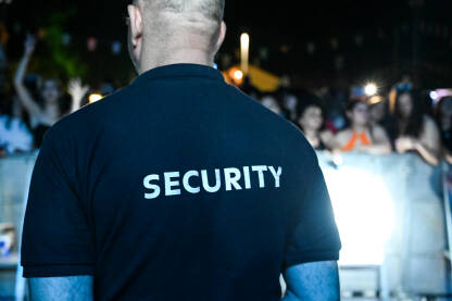 Zaštitar nosi majicu sa natpisom security. Zaštitar stoji ispred publike tokom muzičkog festivala.