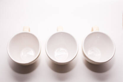 Prazne šoljice za kafu ili čaj poredane paralelno na bijeloj podlozi