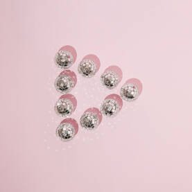 Znak gumba za reprodukciju izrađen od sjajnih disko kugli na pastelno ružičastoj pozadini.