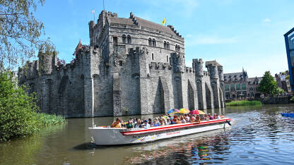 Gent, Belgija: Dvorac uz riječni kanal u središtu grada. Turisti na brodu istražuju grad. Utvrđene kule i zidovi na srednjovjekovnom utvrđenju. Dvorac Gravensteen.