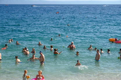 Turisti na moru. Ljudi se kupaju i sunčaju u Jadranskom moru. Ljetni odmor. Grupa turista na plaži tokom toplog ljetnog dana. Makarska, Hrvatska.