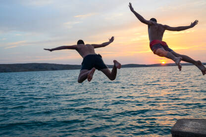 Mladići skaču u more. Ljudi skaču u vodu na zalasku sunca.