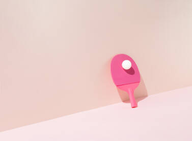 Roze reket za stolni tenis s bijelom lopticom naslonjen na zid.