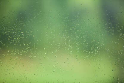Na fotografiji je prozor sa kapima od kiše.Pozadina je zamucena i zelene je boje.