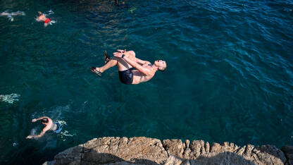 Mladić skače u more. Muškarac pravi salto iznad vode.