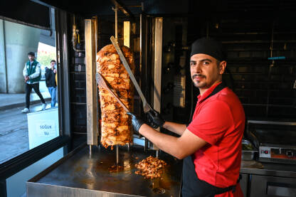 Kuhar priprema i reže doner kebab na vertikalnom ražnju. Čovjek reže meso za velikim noževima. Popularna ulična hrana porijeklom iz Turske.