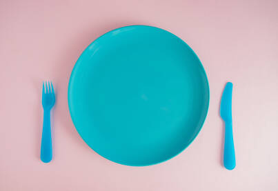 Nož, viljuška, tanjir svijetloplave boje na pastelnoj roze podlozi.