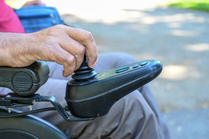 Osoba sa invaliditetom upravlja kolicima. Invaliditet. Čovjek koristi džojstik za vožnju električnih invalidskih kolica, izbliza.