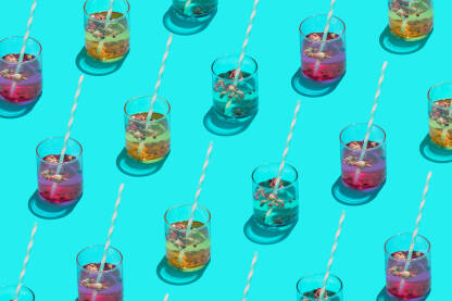 Koktel čaše u bojama s papirnim slamkama na plavoj pozadini.