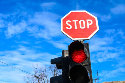 Znak stop i crveno svjetlo na semaforu na raskrsnici. Crveni znak za zaustavljanje na cesti. Saobraćajni znak uz ulicu u gradu.
