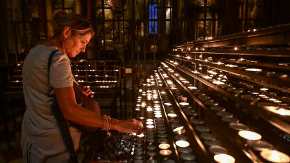 Žena pali svijeću u katedrali. Vjernica sa svijećom u crkvi.