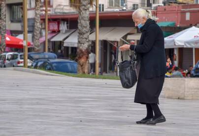 Starija žena stoji na ulici sa maskom na licu.