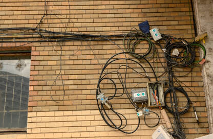 Žice i kablovi na fasadi zgrade Žice od telefona, interneta, kablovske televizije i drugih servisa umotani u veliko klupko na fasadi zgrade. Kablovi na ulazu u zgradu.